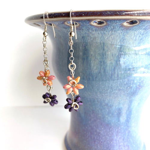 Two beaded flowers dangle along a silver chain. Sweet and dainty.  Collection: Hope in Solitude Color: Pink and purple Drop Length: 2 1/2 inches Metals: .925 Sterling Silver ear wires, mixed metal  