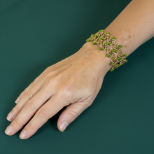 Load image into Gallery viewer, A close-up of a person's hand and wrist wearing a wide beaded bracelet with green superduos and gold seed beads, resting on a green surface.

