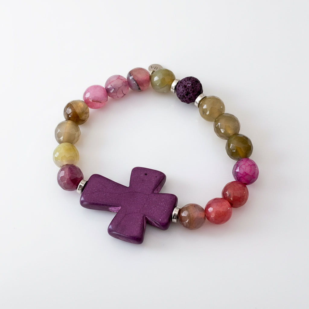 Beaded bracelet in hues of green to purple with a large purple cross as the focal