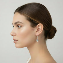 Load image into Gallery viewer, Woman wearing silver heart-shaped earrings against a neutral background
