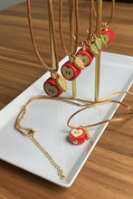 Load image into Gallery viewer, Necklaces with apple-shaped pendants on a white plate and wooden surface
